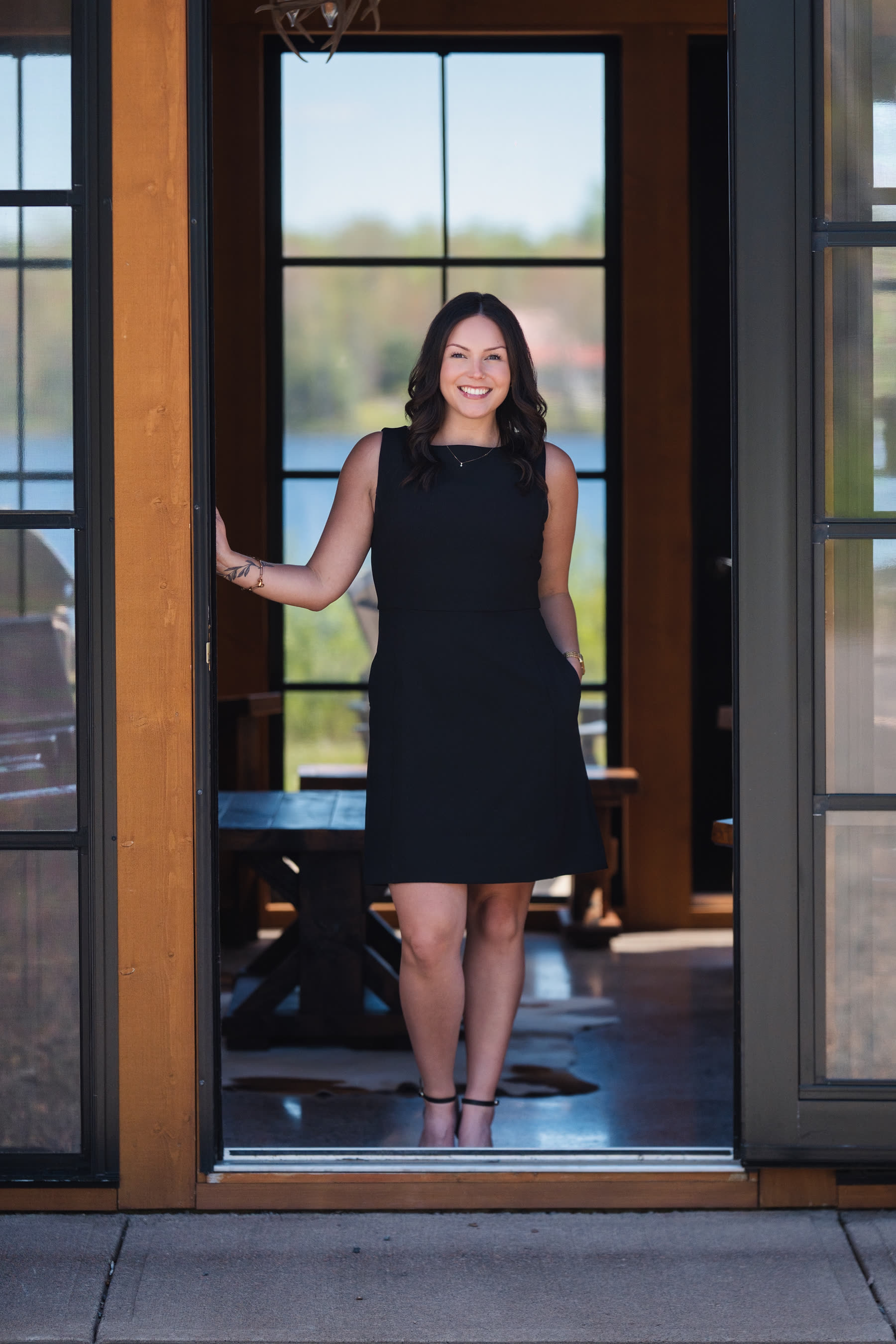 Samantha Johnson standing in the open doorway of a home, with a lake view through the windows behind her.