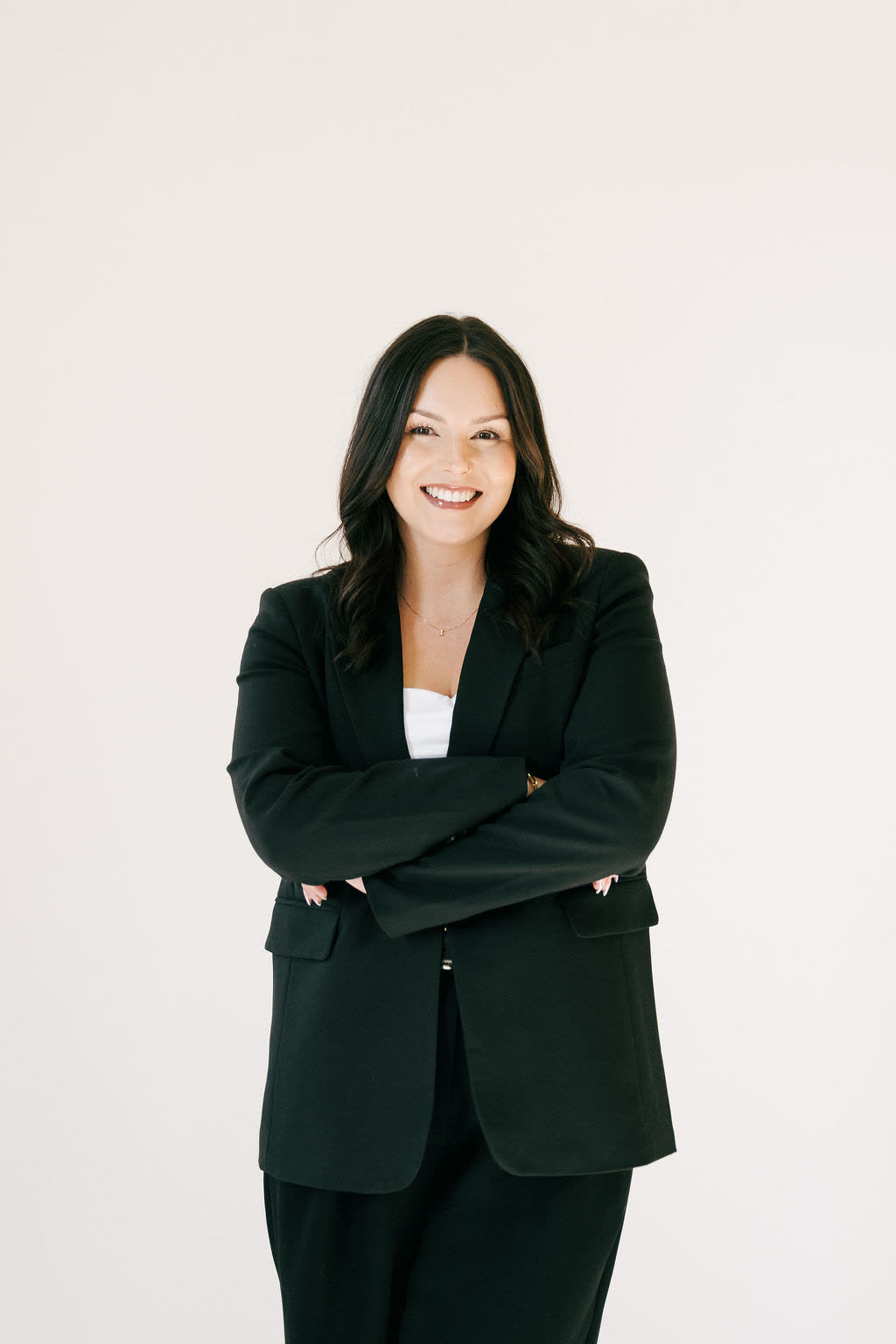 Samantha Johnson smiling with her arms folded, wearing a black suit.