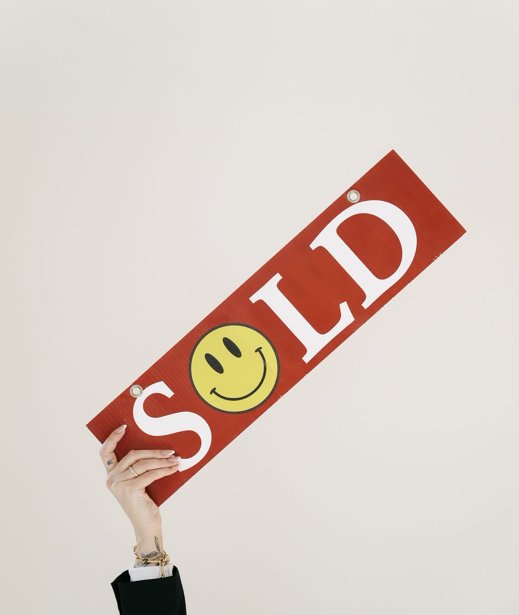 A hand holding up a red SOLD sign with a smiley face.